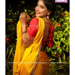 Smiling woman in a vibrant yellow saree with red blouse, showcasing traditional Indian attire.