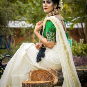 Elegant woman wearing a traditional green and white saree sitting outdoors.