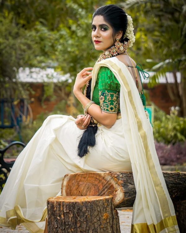 Elegant woman wearing a traditional green and white saree sitting outdoors.