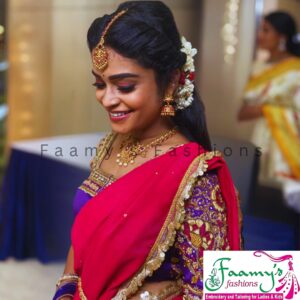 Smiling bride in a red saree with purple embroidered blouse, adorned with traditional gold jewelry